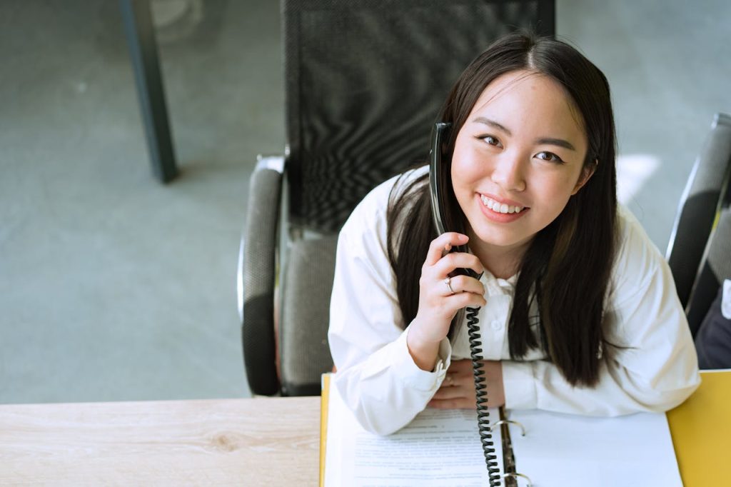 Smiling woman in a white shirt talking on the phone while sitting at an office desk.